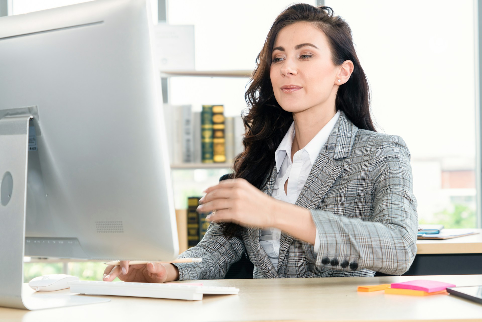 Professional woman in a gray plaid blazer working intently at a computer desk.