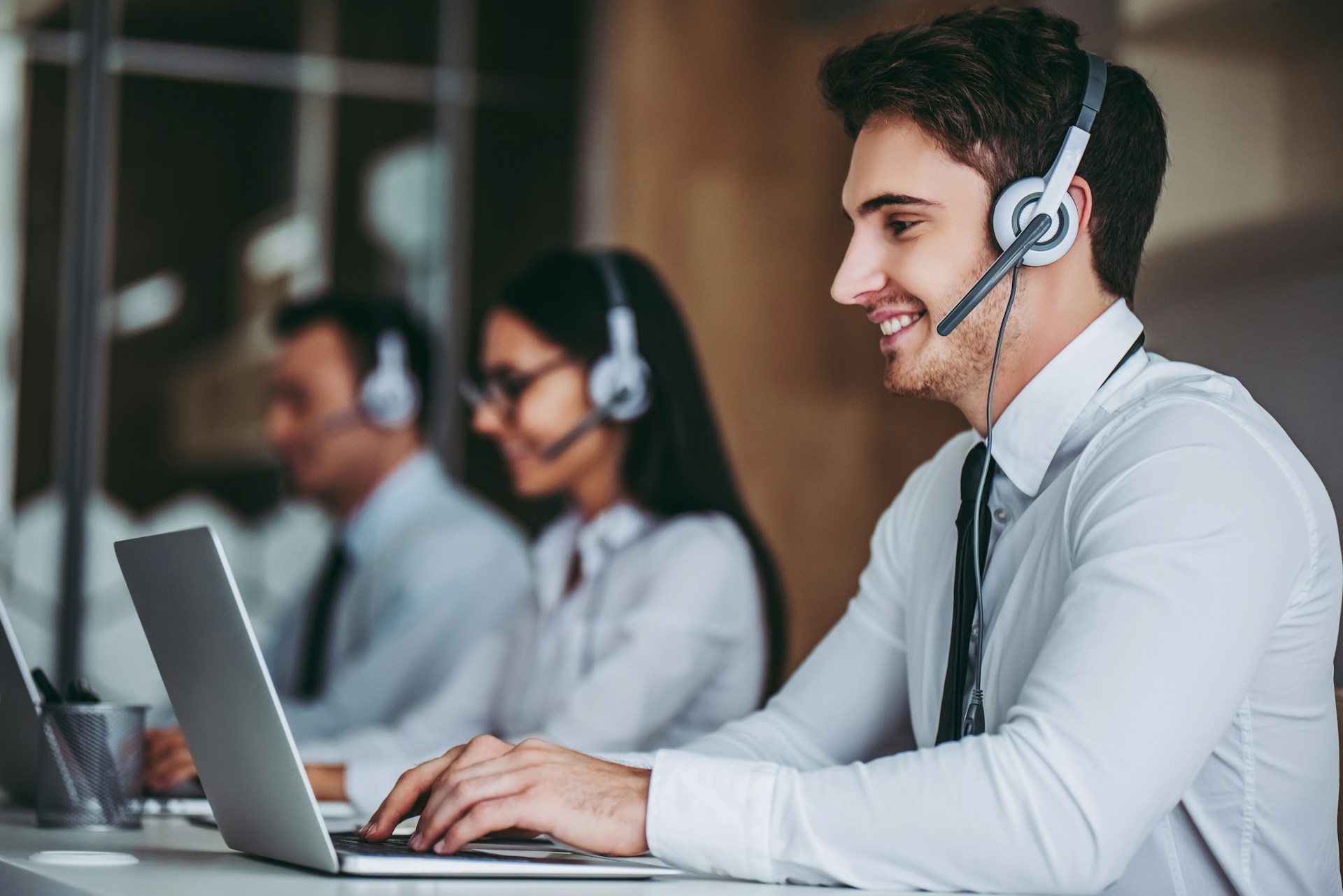 Three customer service agents in headsets working on laptops in a bright office space.